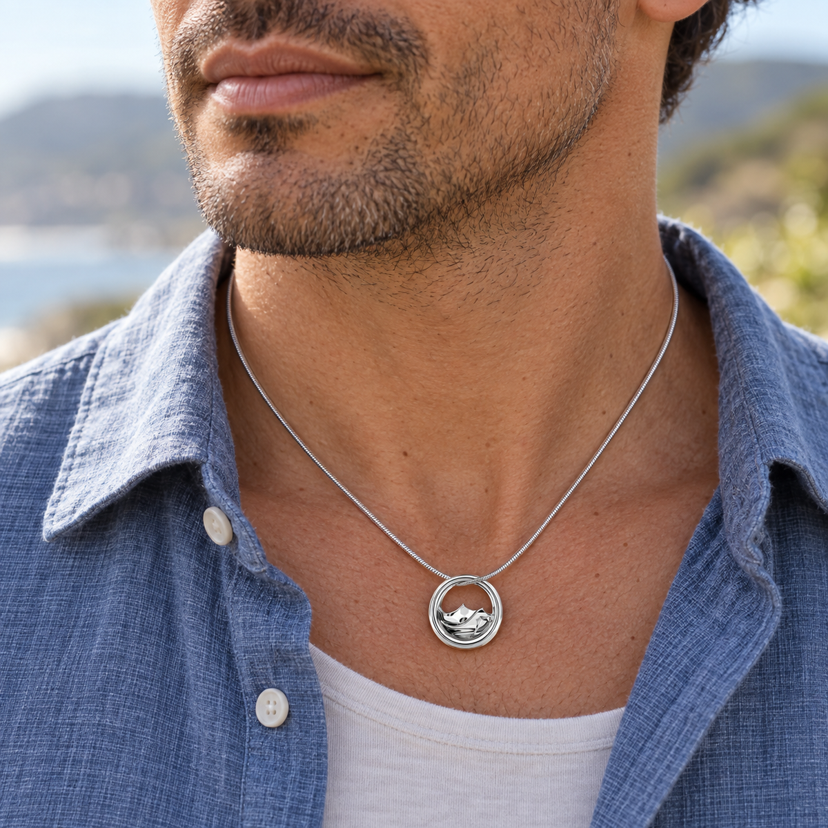 Sterling silver Mountains of Memories pendant worn on a silver snake chain with a blue linen shirt